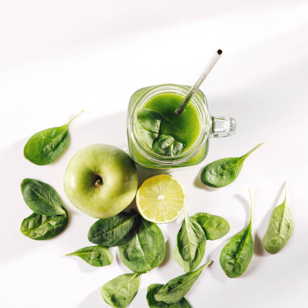 Healthy green vegetable juice with spinach and green fruits and vegetables on white table. 