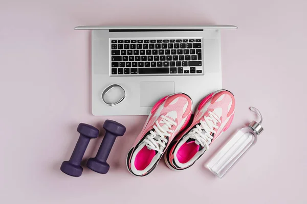 Laptop with fitness sports equipment and sneakers on a pink background.  Home online workout. Top view, flat lay
