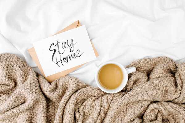 Stay Home, quarantine. warning poster and Cup of coffee on bed with warm plaid. Copy space. Flat lay, top view