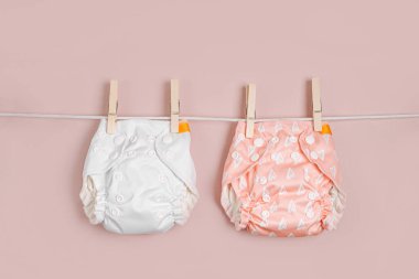 Yeniden kullanılabilir bez bebek bezleri çamaşır ipinde kuruyor. Pembe arka planda çevre dostu bezler. Sürdürülebilir yaşam tarzı. Sıfır atık.