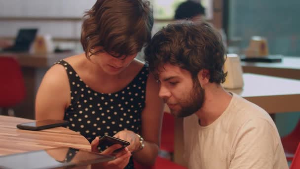 Una Pareja Joven Habla Una Aplicación Una Cafetería Mirando Teléfono — Vídeo de stock