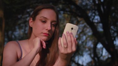 So Paulo 'daki park günbatımında akıllı telefon kullanan Brezilyalı bir kadın.