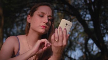 So Paulo 'daki park günbatımında akıllı telefon kullanan Brezilyalı bir kadın.