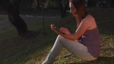 So Paulo 'daki park günbatımında tablet kullanan Brezilyalı bir kadın.