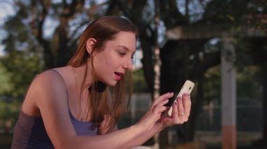 So Paulo 'daki park günbatımında akıllı telefon kullanan Brezilyalı bir kadın.