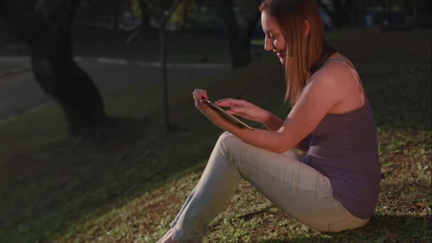 Uma mulher brasileira usando tablet no pôr do sol do parque em So Paulo — Vídeo de Stock