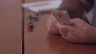 Orta yaşlı Brezilyalı bir adam evin faturalarını ödemek için para sayıyor.