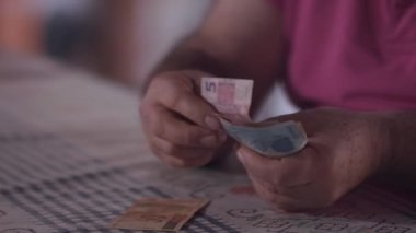Orta yaşlı Brezilyalı bir adam evin faturalarını ödemek için para sayıyor.