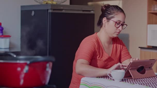 一个女人一边喝咖啡一边在厨房中央的电脑上工作 — 图库视频影像