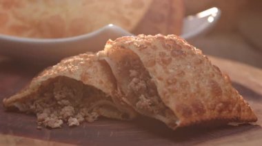 Tabakta kızartılmış hamur işi ve tahtada ikiye bölünmüş etli börek.