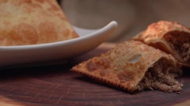 Tabakta kızartılmış hamur işi ve tahtada ikiye bölünmüş etli börek.