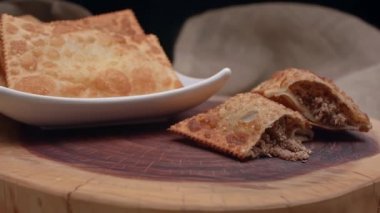 Tabakta kızartılmış hamur işi ve tahtada ikiye bölünmüş etli börek.
