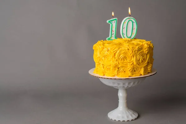 Yellow frosted cake with a 10 candle on top and gray background