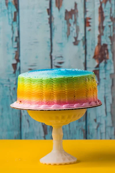 Rainbow frosted cake with yellow table and blue background