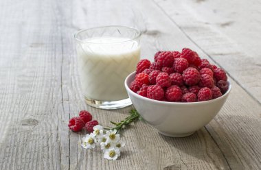 yanında bir bardak süt, papatya çiçekleri matricaria, mükemmel renkli yaz arka plan ağaç doku, lezzetli hafif Kahvaltı, Natürmort ile süslenmiş sulu olgun ahududu dolu kase