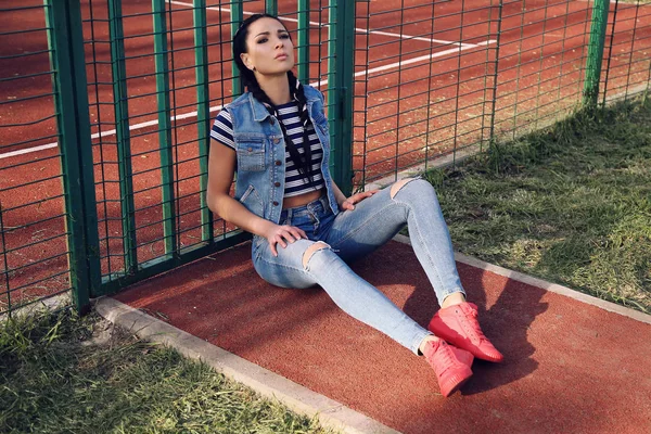 Beautiful girl with dark hair in jeans clothes posing at stadium — Stock Photo, Image