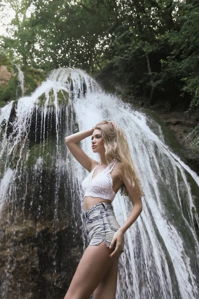 Schönes Mädchen mit blonden lockigen Haaren posiert in der Nähe des Wasserfalls — Stockfoto