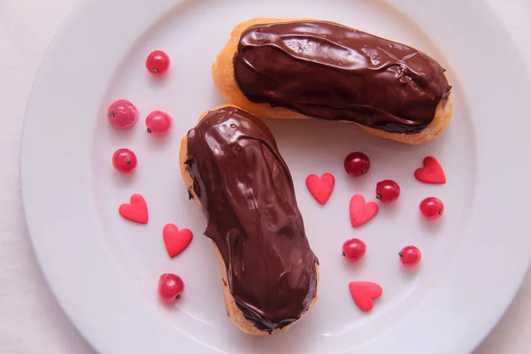 Pasteles de chocolate en plato sobre fondo blanco espolvoreado con bayas de grosella roja y corazones — Foto de Stock