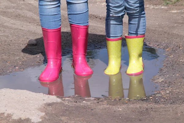 Childrens legs in jeans in rain rubber boots standing in a puddle in the sun — Stock Photo, Image