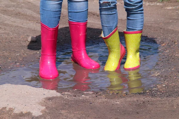 Pernas de crianças em calça em botas de borracha de chuva que estão em uma poça no sol — Fotografia de Stock