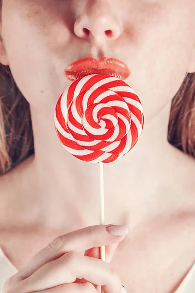 Spiral lollipop in a female hand is pressed against the bright red lips. Close-up — Stock Photo, Image