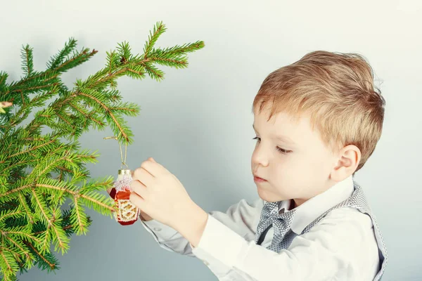 Five-year-old red-haired boy hangs the decor on a branch of a Christmas tree. Preparation for Christmas and New Year.