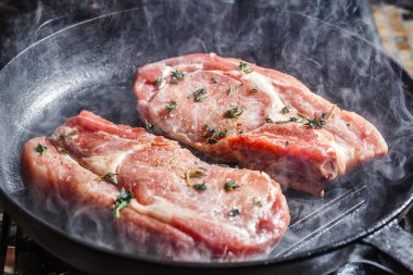 Doğal Domuz pirzola tecrübeli biber, tuz, sarımsak ve kekik, ızgara tavada kızartma ile yukarıda duman yükselir
