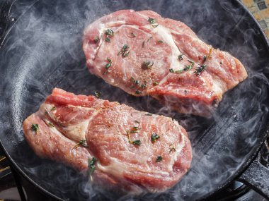 Doğal Domuz pirzola tecrübeli biber, tuz, sarımsak ve kekik, ızgara tavada kızartma ile yukarıda duman yükselir