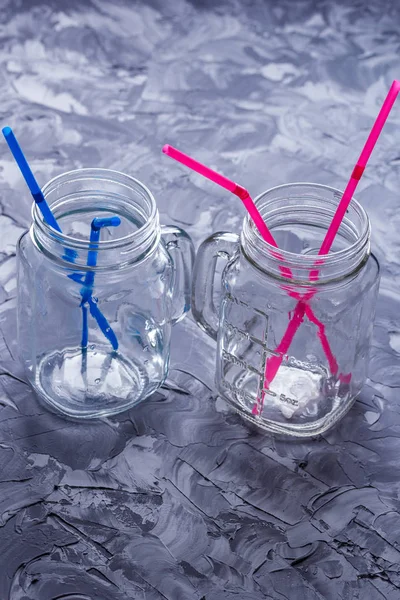 Empty drinking jars with colored drinking straws on a concrete table