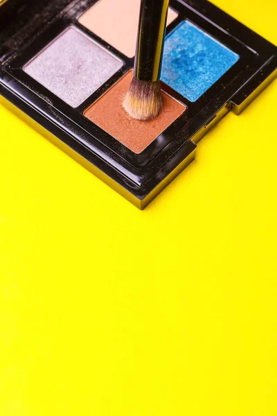 Brush for make-up over a set of eye shadow on yellow background. Copy space