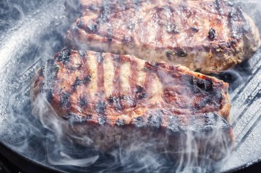 Domuz biftek biber, tuz, sarımsak ve kekik, ızgara tavada kızartma ile yukarıda duman yükselir