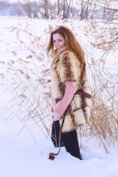 Mooie jonge vrouw in bont vest tegen de achtergrond van een winterlandschap — Stockfoto