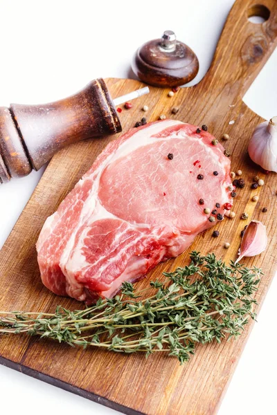生の豚肉のステーキ 新鮮なタイム ニンニク 唐辛子豆 白い背景のクローズ アップに木製のまな板にペッパーミルの束 調理肉 マリネのレシピのコンセプト — ストック写真