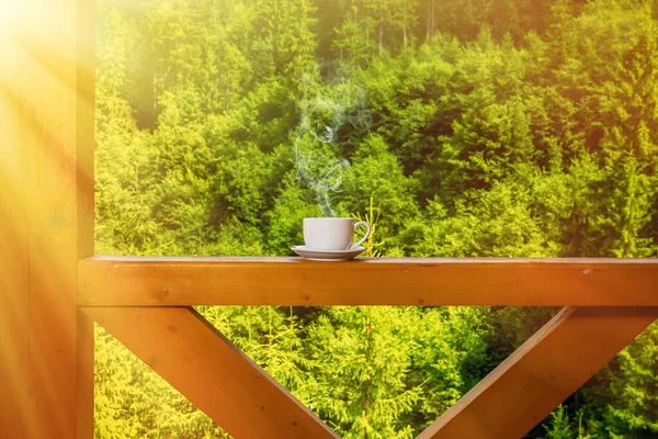 El vapor se eleva sobre una taza con una bebida caliente en una cubierta de madera en el fondo del bosque en un día soleado de verano. Concepto camping —  Fotos de Stock