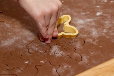 Zencefilli Noel kurabiyeleri yapmak için özel kalıplar kullanarak hamurdan figürler kesmek. Çocukların elleri, yakın plan. Ev ve aile tatil konseptine hazırlanıyor.