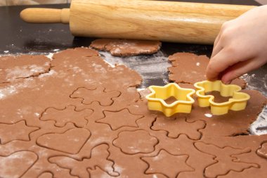 Zencefilli Noel kurabiyeleri yapmak için özel kalıplar kullanarak hamurdan figürler kesmek. Çocukların elleri, yakın plan. Ev ve aile tatil konseptine hazırlanıyor.