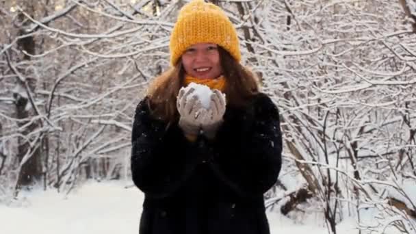 Een gelukkig meisje loopt door het winterbos, glimlacht, heeft een goed humeur, speelt met sneeuw, blaast uit en gooit sneeuwvlokken op de achtergrond van sneeuw — Stockvideo