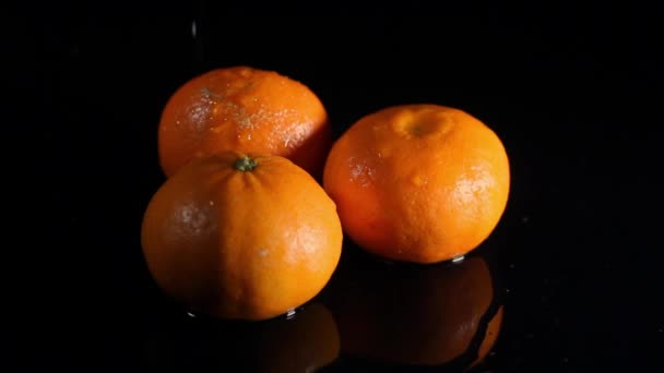 Las mandarinas brillantes jugosas anaranjadas sobre la superficie negra del espejo bajo las gotas de agua. Fruta fresca, estilo de vida saludable, concepto de piel juvenil — Vídeo de stock