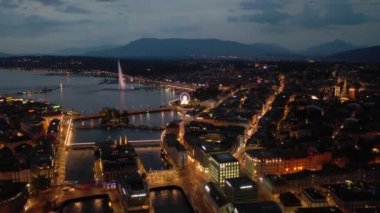 Night time 4k footage of illuminated Geneva aerial riverscape panorama with huge fountain, Switzerland  