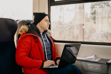 Trenle gidiyor ve pencerenin önünde izlerken laptop ile kırmızı ceket bir adam