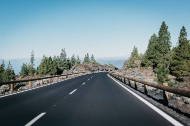 Kayalar ile o çok yakın bulutlar sağa yeşil çam ağaçlarının arasında karayolu gider. Teide Milli Parkı. Tenerife