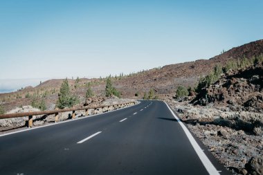 Sağdaki bulutlar yakınındaki taş yeşil çam ağaçları ile karayolu geçer. Teide Milli Parkı. Tenerife
