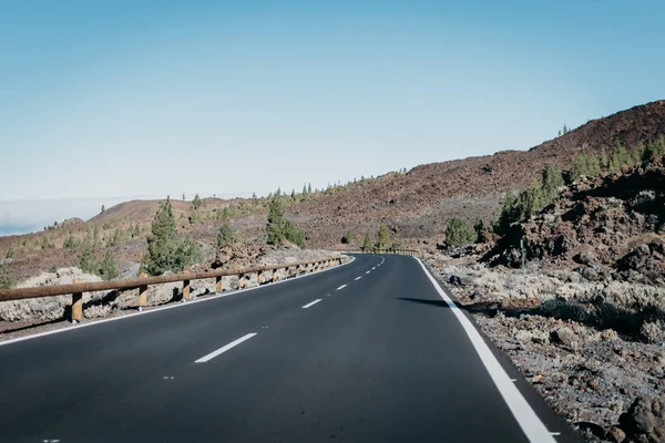 Sağdaki bulutlar yakınındaki taş yeşil çam ağaçları ile karayolu geçer. Teide Milli Parkı. Tenerife