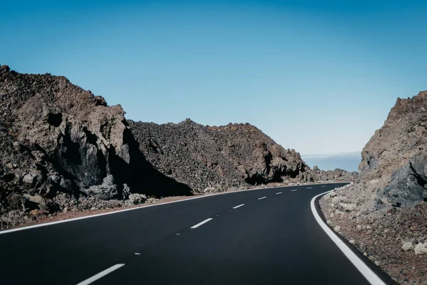 Highway goes straight between huge rocks to the right near the clouds. Teide National Park. Tenerife