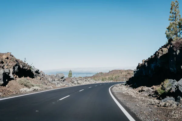 Otoyol kayalıklardan yakınındaki bulutlar sağa yeşil çam ağaçları ile arasında gider. Teide Milli Parkı. Tenerife