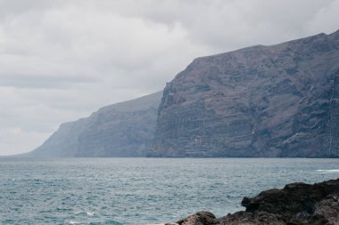 Los Gigantes kayalıklarla ön siyah volkanik kayalar ile. Tenerife