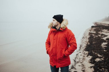 Kırmızı parka, siyah şapka ve kot güçlü adam sahilde duruyor. Jurmala Letonya