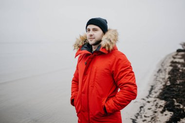 Kırmızı parka ve siyah şapka güçlü adam sahilde duruyor. Jurmala Letonya
