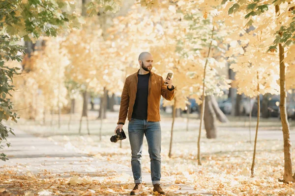 수염을 대머리의 작가가 스웨이드 파란색 청바지 부츠를 공원에 카메라와 스마트폰을 — 스톡 사진