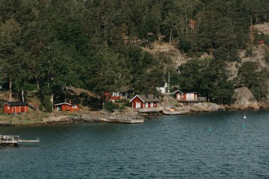 Güneşli bir günde, kayalık sahil kıyısında ormandaki yaylalar arasında bir köy..